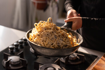 Professional chef cook making Italian Tagliatelle pasta with mushrooms and cream at kitchen gas...