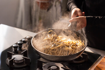 Professional chef cook making Italian Tagliatelle pasta with mushrooms and cream at kitchen gas stove in wok pan. Flying pasta levitation in motion.