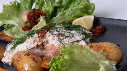 Close-up of appetizing oven baked potatoes and baked salmon in foil. Served on gray plate. Excellent image for homemade food banners and advertisements.