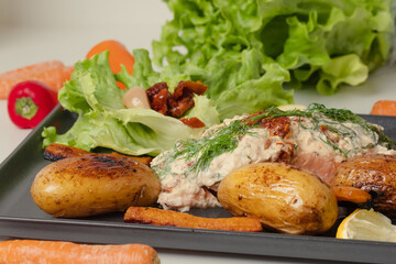 Appetizing oven baked salmon, potatoes decorated with fresh salad and dried tomatoes. Served on gray plate. Light background. Excellent image for homemade food banners and advertisements.
