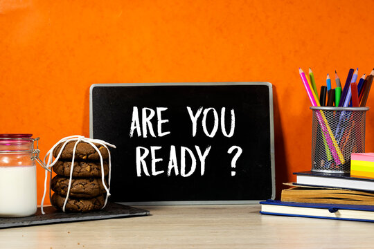 Back to school concept - are you ready question on blackboard with pencil-box and books, notebook and sticky note, milk and cookies on wooden table