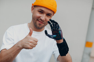 Young disabled man with artificial prosthetic hand put on finger nozzle pad and thumbs up gesture