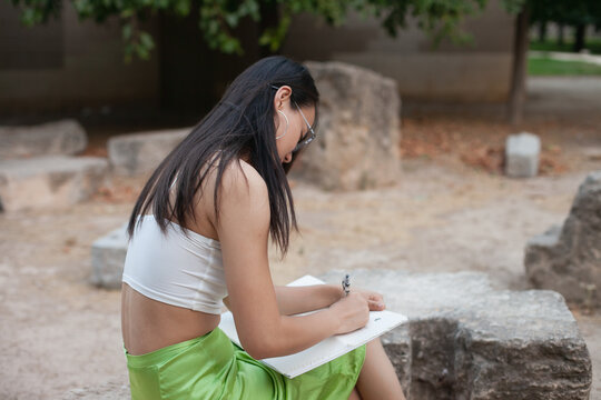 Young asian girl student wearing glasses doing homework on campus or in the park. Female education in Asia. International exchange student programs for Chinese girls.