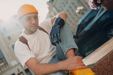 Young disabled man with artificial prosthetic hand in casual clothes at city street