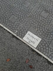 Marble plaque on asphalt and geometric pavement with the words PRIVATE PROPERTY in Italian seen...