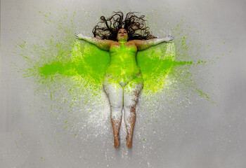 Sexy, plus size, fat, overweight, chubby woman, green, yellow color painted decorative. Long brunette curly hair lying on the white designed studio floor, top view