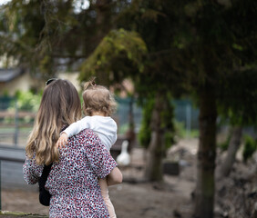 mother holds toddler in her arms, village natural background - obrazy, fototapety, plakaty