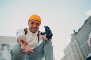 Young disabled man with artificial prosthetic hand in casual clothes at city street
