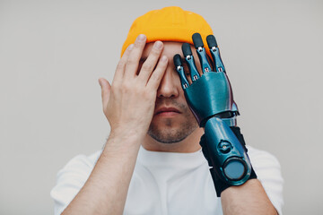 Young disabled shy man close face with artificial prosthetic hand in casual clothes