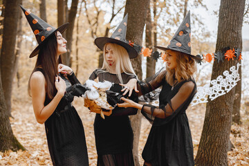 Naklejka premium Three black witches in forest on Halloween holding a cauldron
