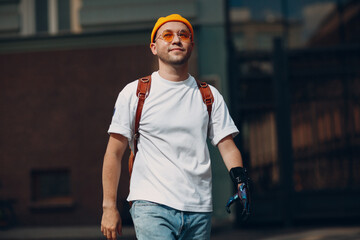 Young disabled man with artificial prosthetic hand in casual clothes and backpack walking at sunny...