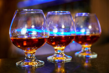 Three cognac glasses with cognac on the bar