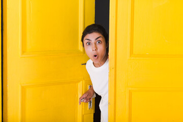 Young surprised indian woman peeking through yellow open door