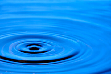 Splash drop of water with diverging water circles, on blue background.