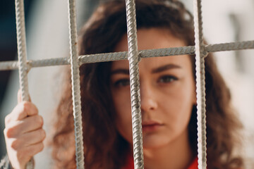 Young brunette curly woman in orange suit behind jail bars. Female in colorful overalls portrait