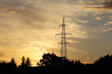 Silhouette of high voltage tower with electrical wires on background of sunset sky and dark clouds. Electricity transmission lines in evening forest, power supply concept