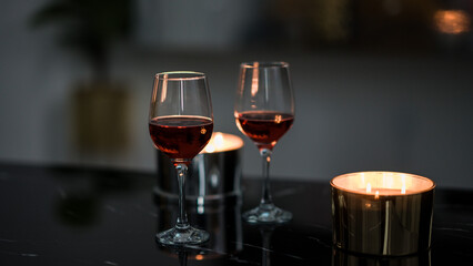two glasses of red wine on a black table. Candle in the background