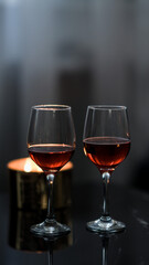 two glasses of red wine on a black table. Candle in the background