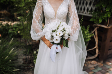 A beautiful bride in a lace dress with a long veil holds a bouquet of white roses close-up. wedding...