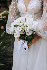 A beautiful bride in a lace dress with a long veil holds a bouquet of white roses close-up. wedding photography.