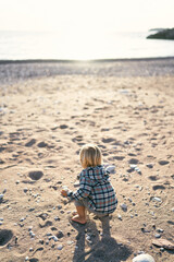 Little girl squatting on the beach. Back view. High quality photo