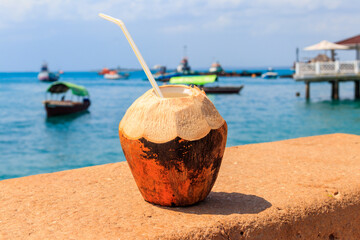 Naklejka premium Fresh tropical coconut cocktail with drinking straw by ocean in Stone Town, Zanzibar, Tanzania