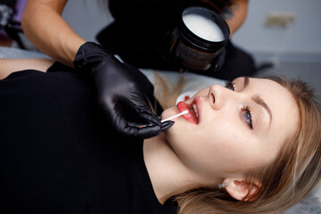 Cosmetologist master apply red permanent lips tattoo for girl - obrazy, fototapety, plakaty