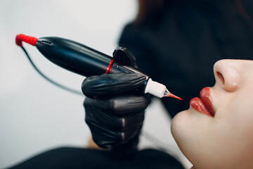 Cosmetologist applying red permanent make up tattoo on female lips. - obrazy, fototapety, plakaty