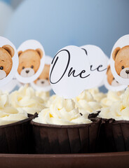 many cupcakes with white cream and toppers with bears and text one