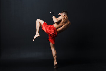 Sportsman muay thai man boxer stance ad knee kick at black background.
