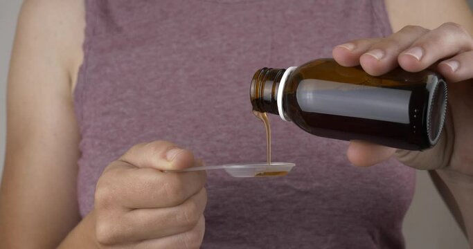 woman pouring cough syrup into a spoon to treat a cold. High quality 4k footage