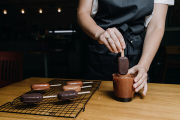 A female confectioner dips an ice cream cake into melted chocolate. Hands close up. Preparation of cupcakes