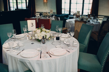 round tables in the restaurant with white tablecloths and white bouquets of flowers decor.