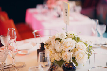 round tables in the restaurant with white tablecloths and white bouquets of flowers decor.
