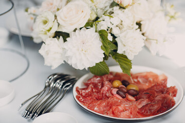 Various cold cuts on a plate with white flowers on table.