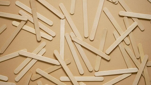Wooden popsicle sticks, scattered on top of a beige background