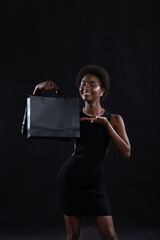 African american woman with afro hairstyle holds black shopping bags. Sale and discounts on market and Black Friday concept.