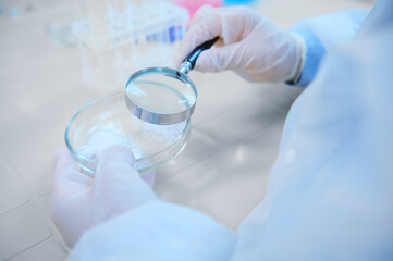 Selective focus: Loupe with magnifying glass in a scientist pharmacologist hands, examining...