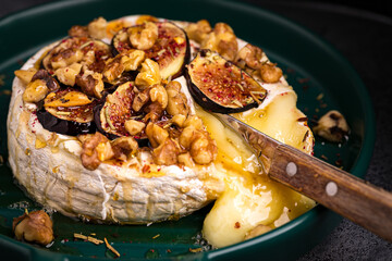  Baked brie with nuts and figs in a green bowl. Knife cuts cheese.