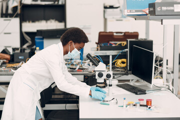 Scientist african american woman in medical face mask and gloves working in laboratory with electronic tech instruments and microscope. Research and development of electronic devices by color black