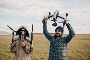 Two men pilots holding quadcopter drone in hands at outside field