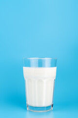 close-up view of white milk in transparent faceted glass. on blue background, side view. Dairy product concept, copy space.