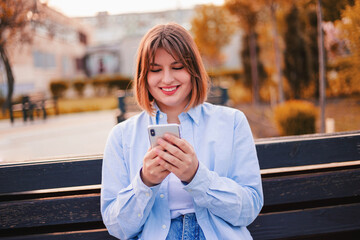 Photo of charming pretty young lady communicating modern gadget sitting bench smiling outside urban city street