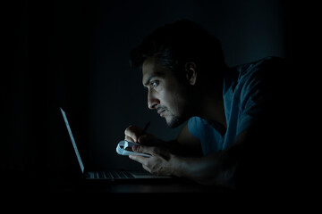 Side view of young handsome man working on laptop at night. Work from home concept