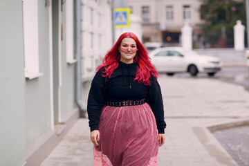European plus size woman. Young red pink haired body positive girl walk at city street outdoors