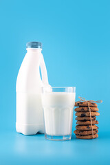 Tasty cocoa cookies with chocolate drops. A bottle and a glass of milk isolated on blue background. flatlay, text space.