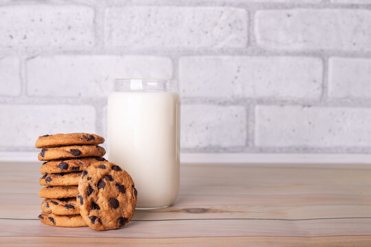 Composition of freshly baked homemade biscuits with chocolate chips. Healthy breakfast concept with glass of milk and cooked cookies on wooden table for overlay on product presentation. - Powered by Adobe