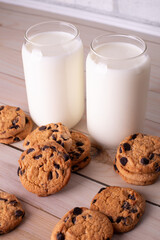 Glasses of fresh milk and brown school chocolate cookies. The cookies with chocolate drops and on a rustic wood kitchen table, with copy space. yummy and tasty