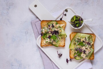 Open Danish smorrebrod sandwiches with chicken salad, fresh cucumber and herbs on a white ceramic board against a light concrete background. Sandwich recipes.