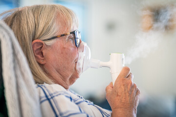 Senior lady breathing through oxygen inhaler at home. Medical and treatment concept. - obrazy, fototapety, plakaty